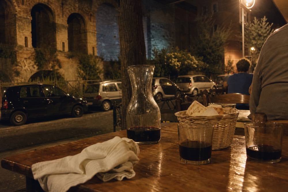 A candlelit trattoria table with a carafe of red wine and bread basket