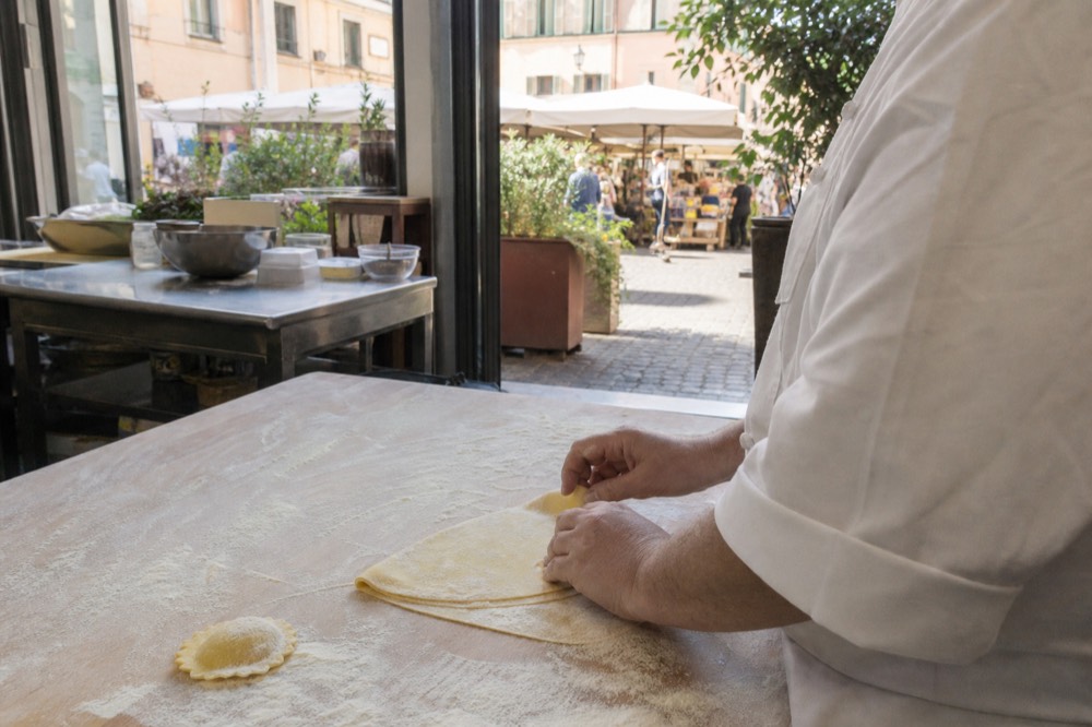 A chef demonstrating how to fold fresh pasta dough on a floured wooden board