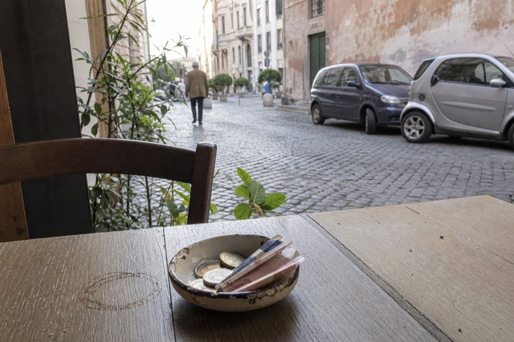 A small ceramic bowl holding a few euro coins and banknotes on a wooden kitchen table