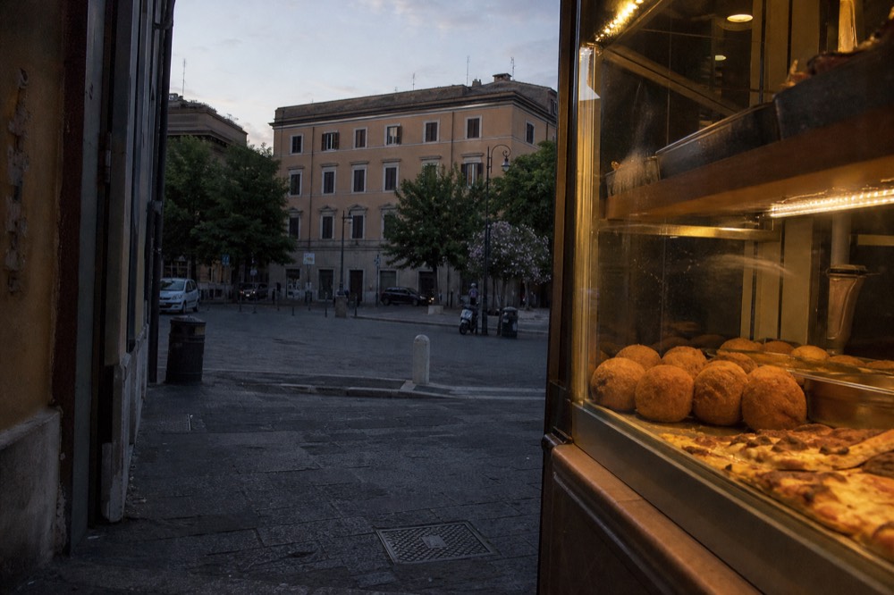 A Roman street food counter displaying fried supplì and pizza slices under a glass case