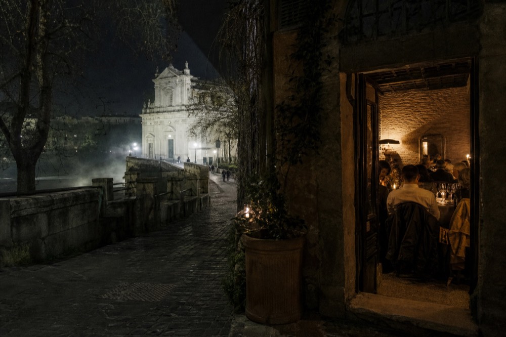 An evening table set with wine glasses, bread and small plates of Roman dishes in a candlelit room