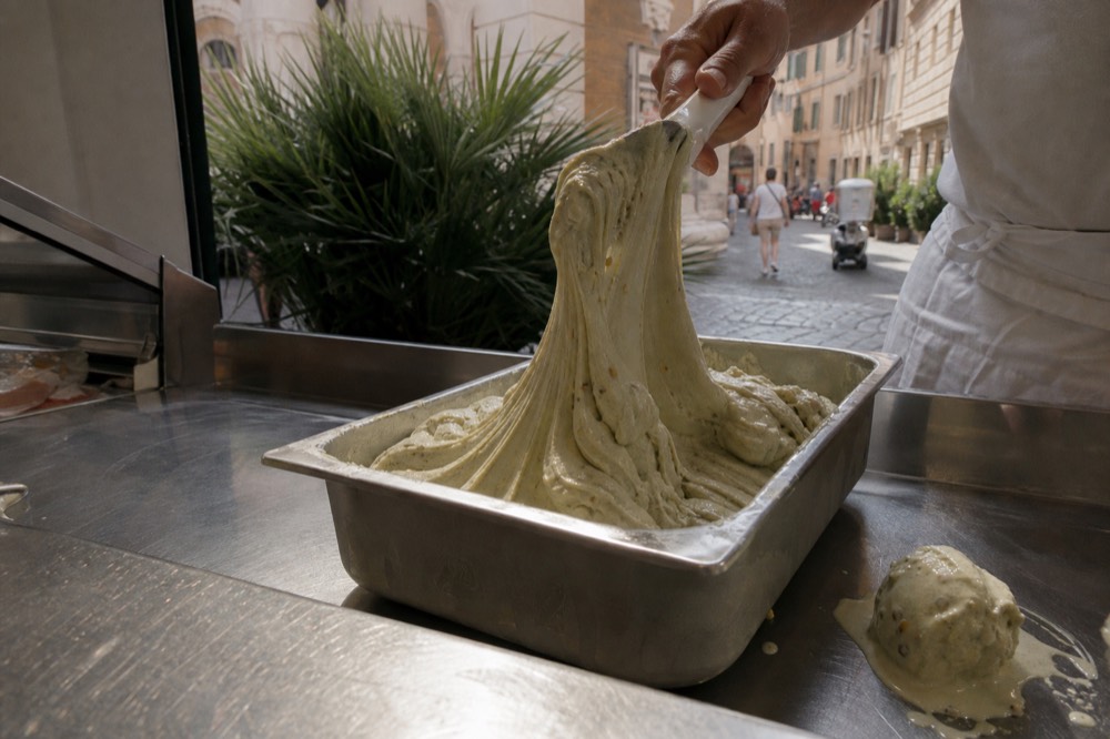 A spatula lifting a ribbon of dense pistachio gelato from a metal tray