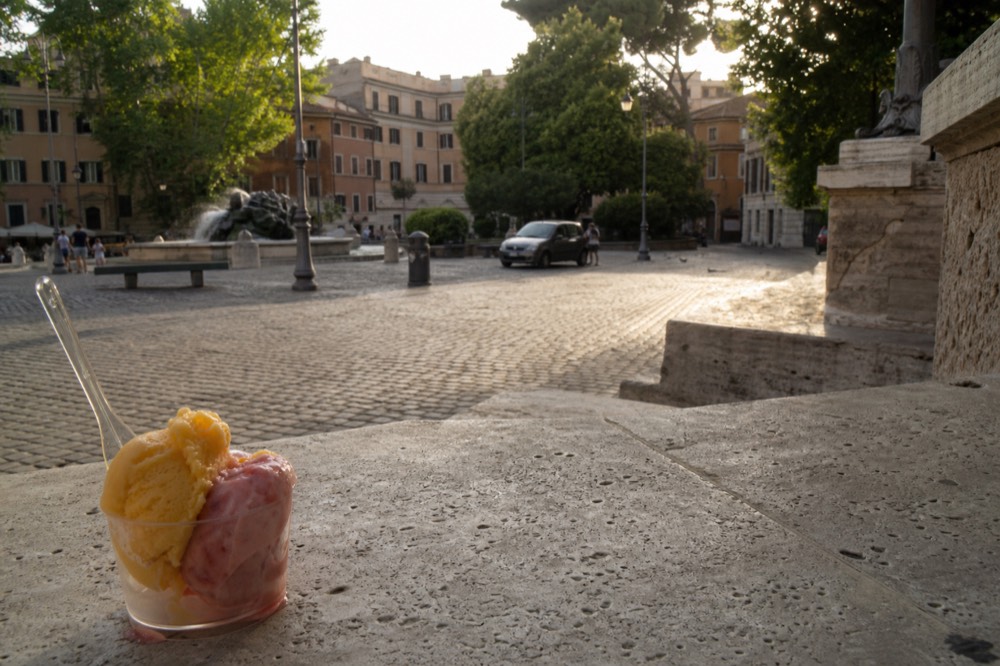 Small clear cup with two scoops of fruit gelato on a marble counter in Rome
