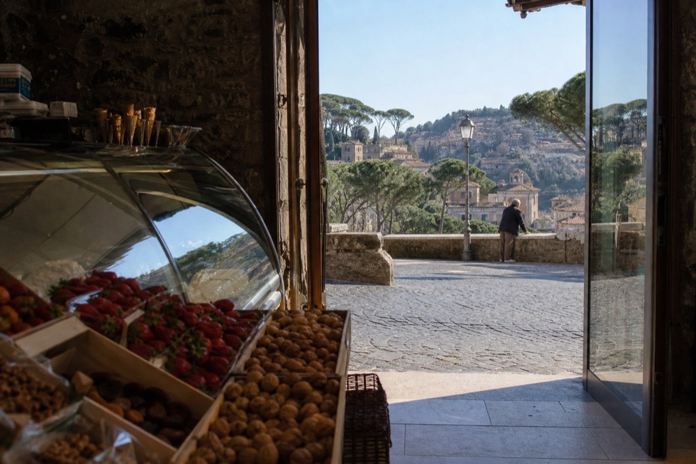 Seasonal fruit trays and nuts displayed beside a covered gelato case in a small Roman shop