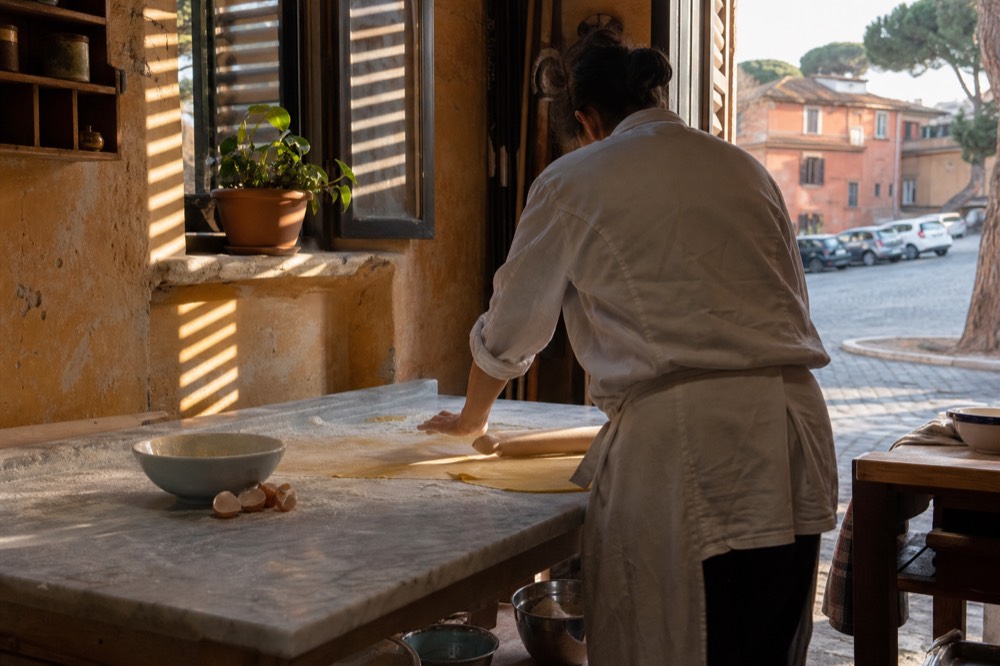 A cook rolling fresh tagliatelle dough on a floured marble surface