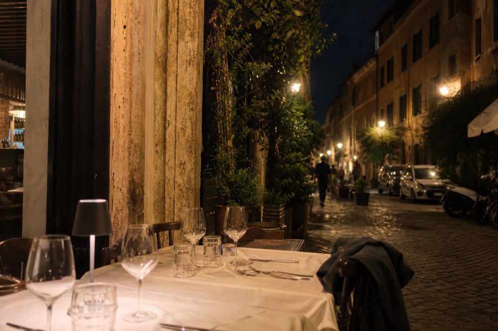 Restaurant tables set for dinner in a lamplit Trastevere alley