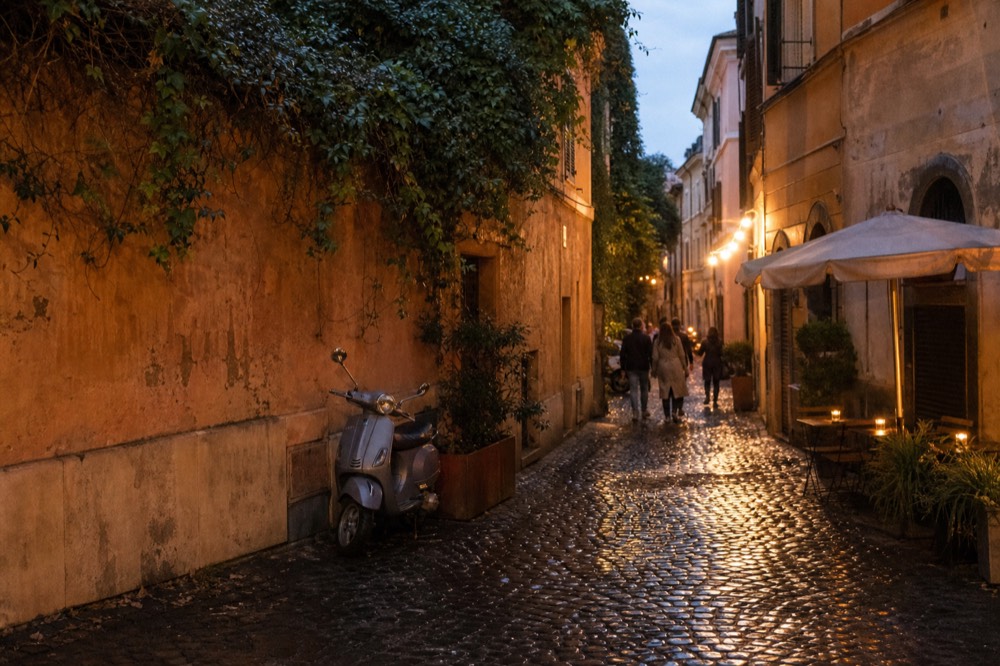 Trastevere lane at dusk with warm restaurant lights reflecting on cobblestones