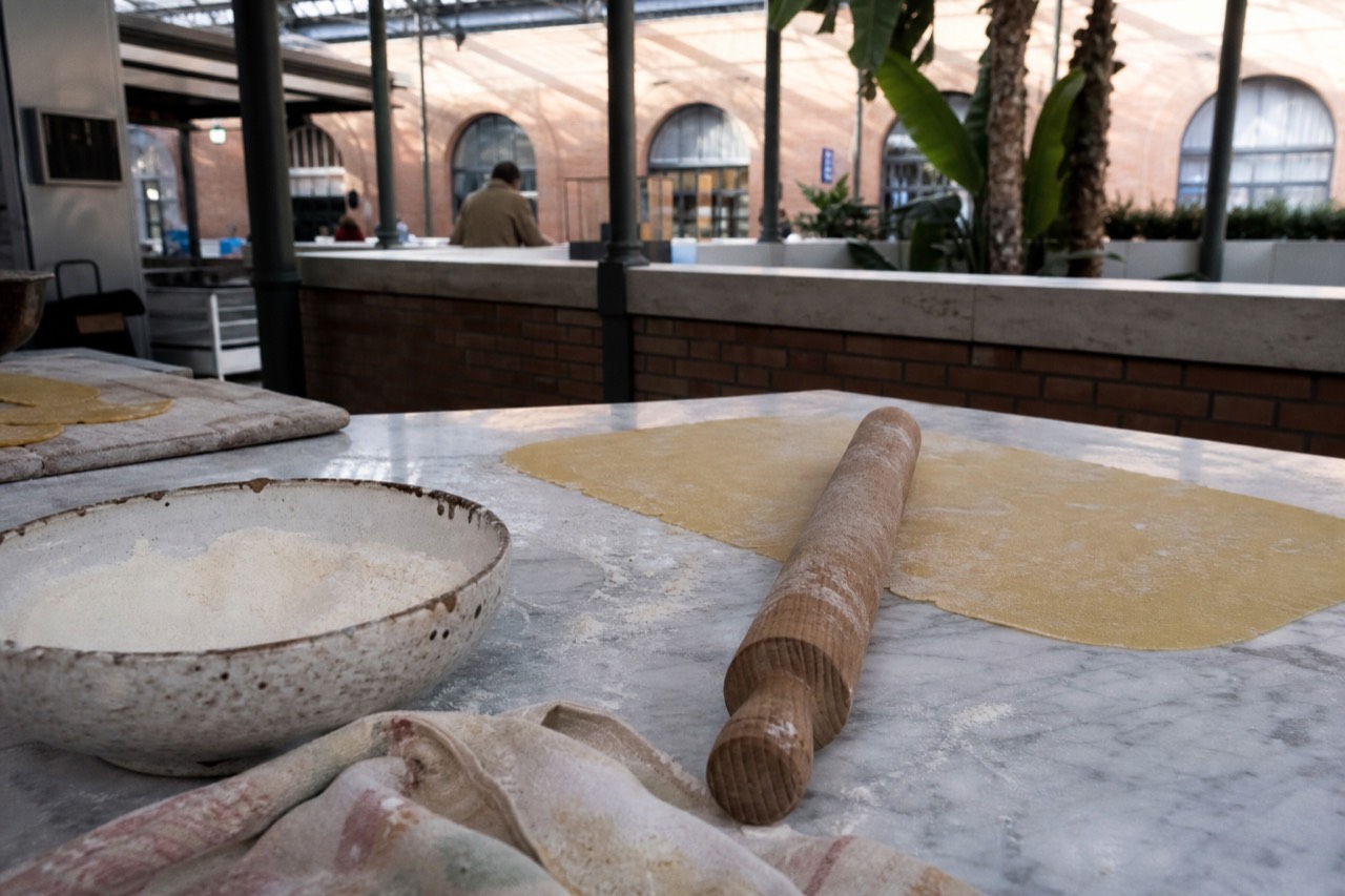 A wooden table set with fresh pasta dough, eggs, and a rolling pin in a sunlit kitchen in Rome