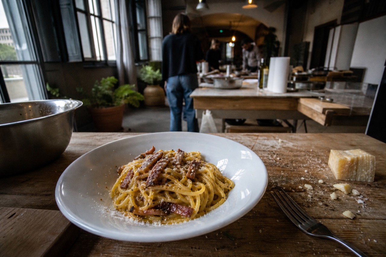 A bowl of spaghetti carbonara with glossy egg sauce, crisp guanciale pieces and coarsely ground black pepper on a rustic wooden table