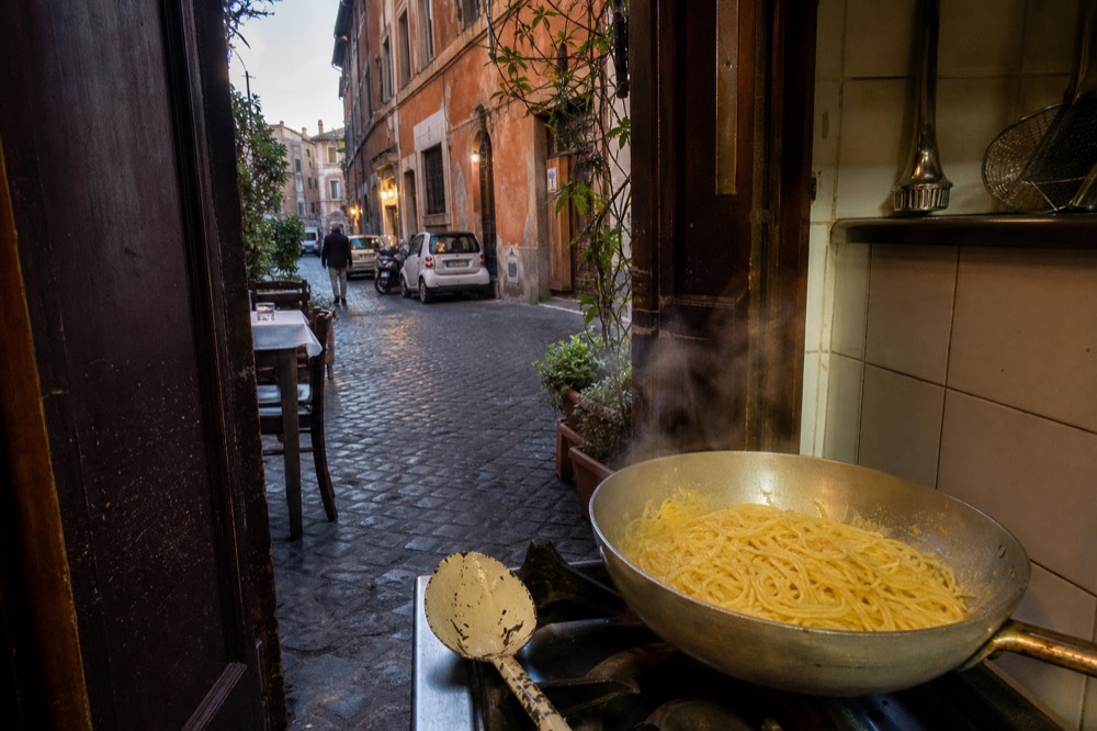 Spaghetti being tossed with egg and cheese in a large pan over gentle heat