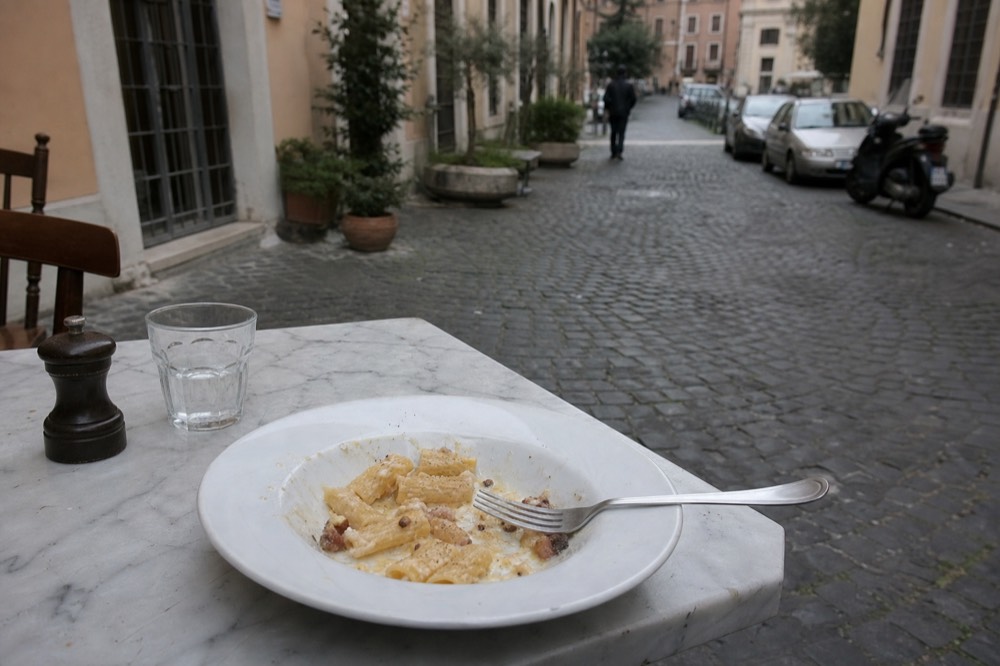 A finished plate of carbonara with cracked pepper and crisp guanciale in a Roman trattoria