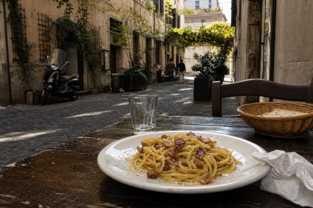 A plate of spaghetti carbonara with crispy guanciale and black pepper on a wooden table