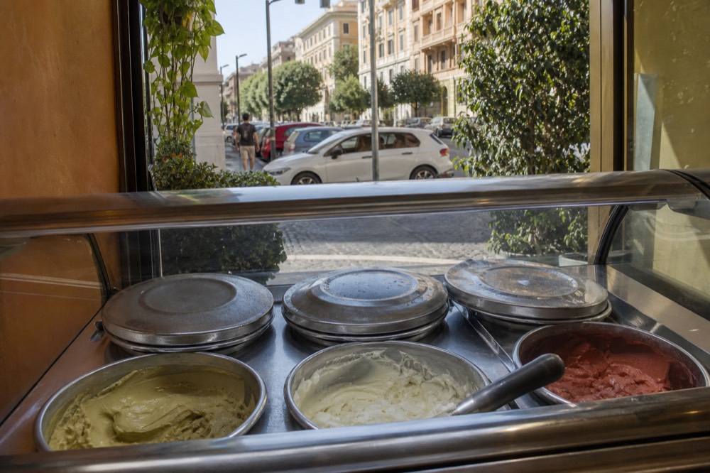 Assorted gelato flavors in covered metal tins inside a Roman gelateria