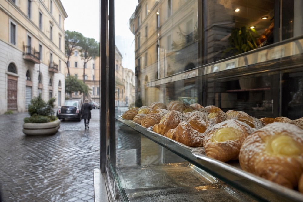 A glass display case in a Roman pastry bar holding cornetti filled with cream and apricot jam