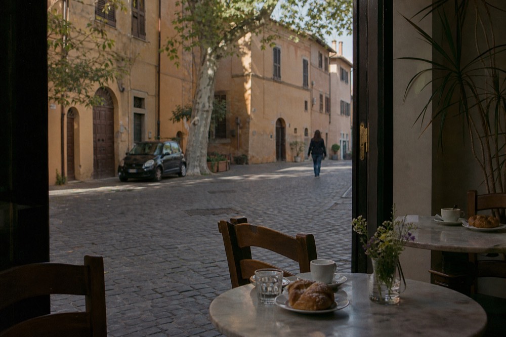 A quiet Roman café interior with small marble tables set with cups and pastries in the morning light
