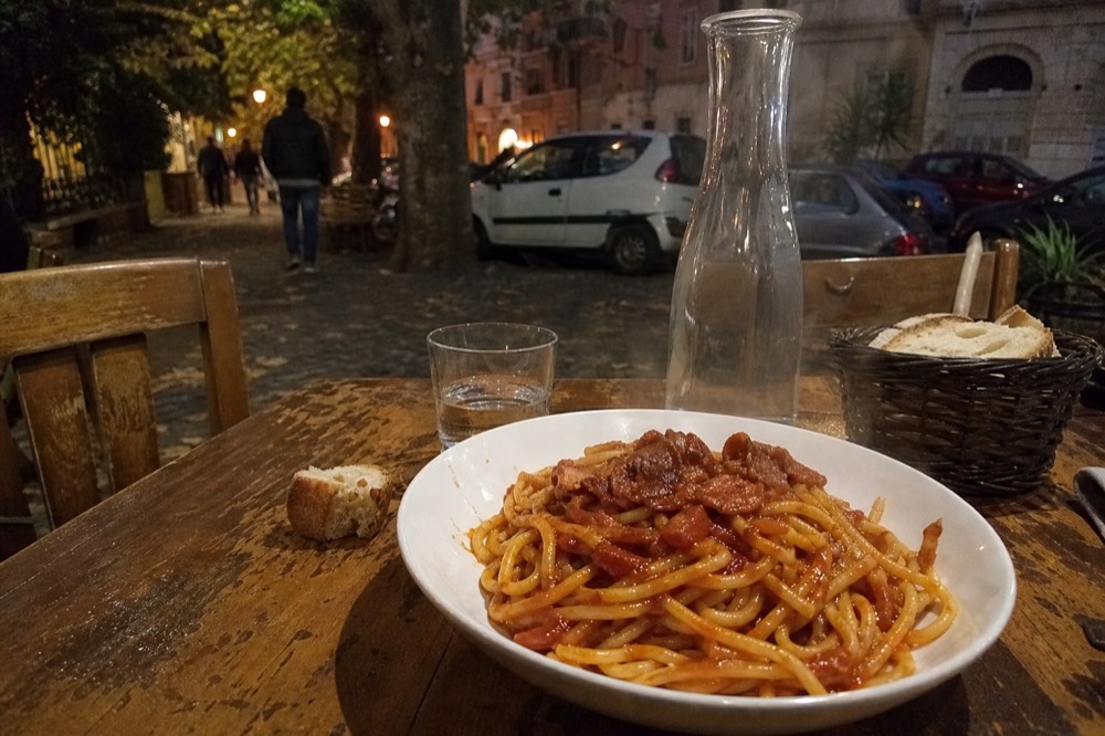 A bowl of bucatini all'amatriciana with tomato sauce and cured pork on a wooden table