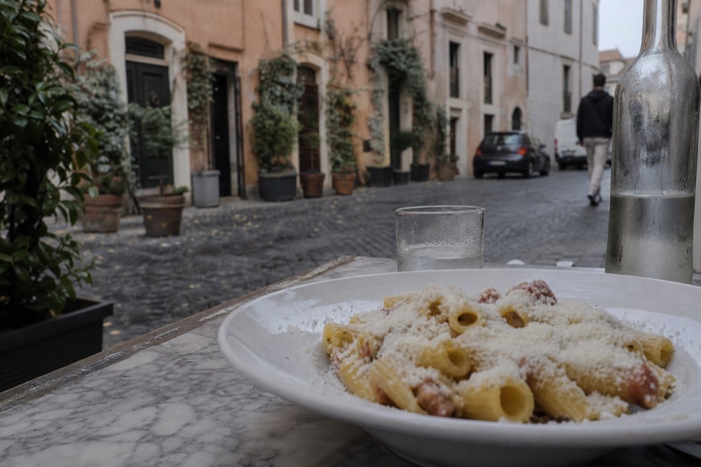 Rigatoni with crispy guanciale pieces and pecorino cheese in a white bowl