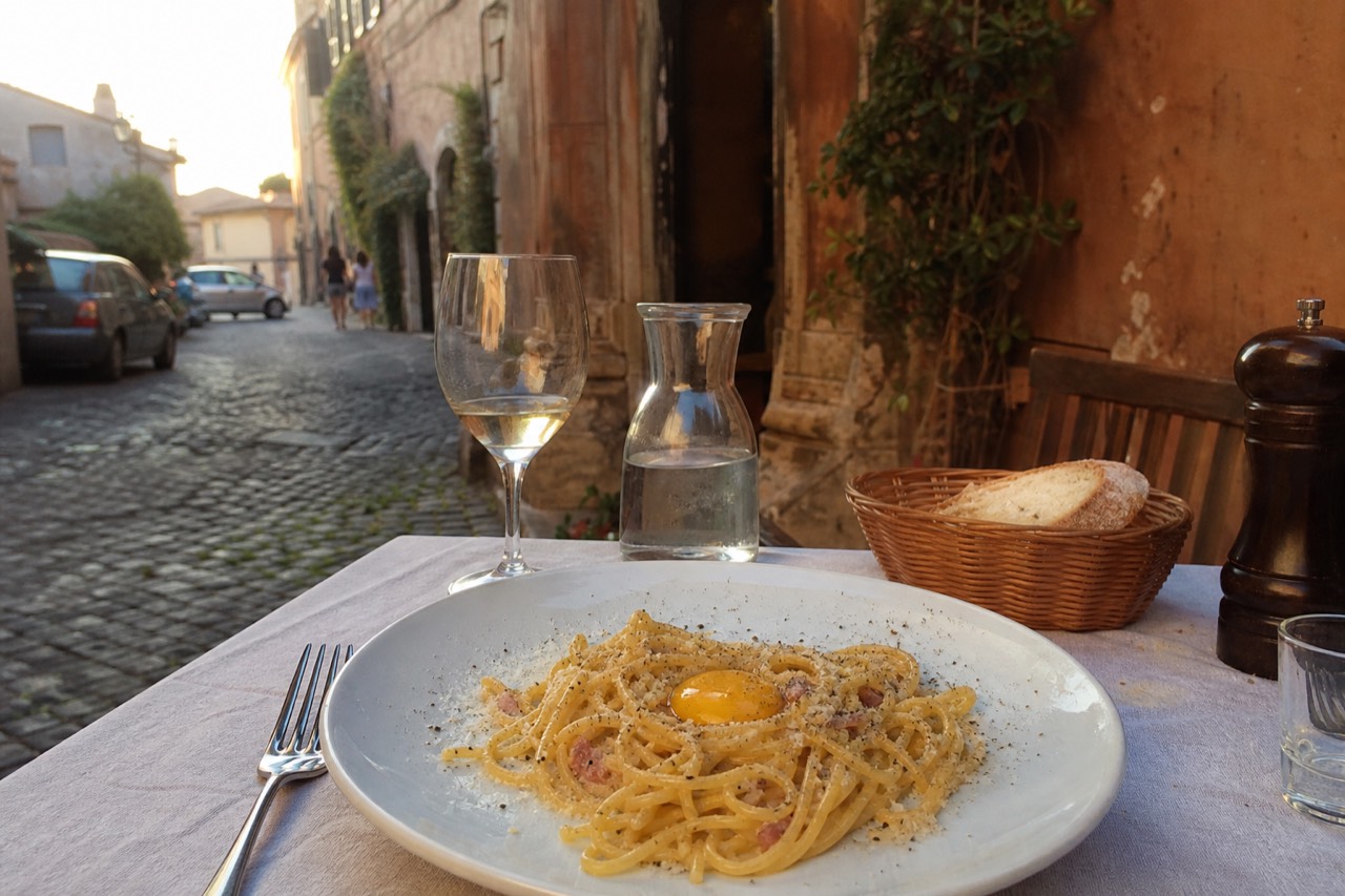 A plate of spaghetti carbonara topped with egg yolk and cracked black pepper on a rustic trattoria table