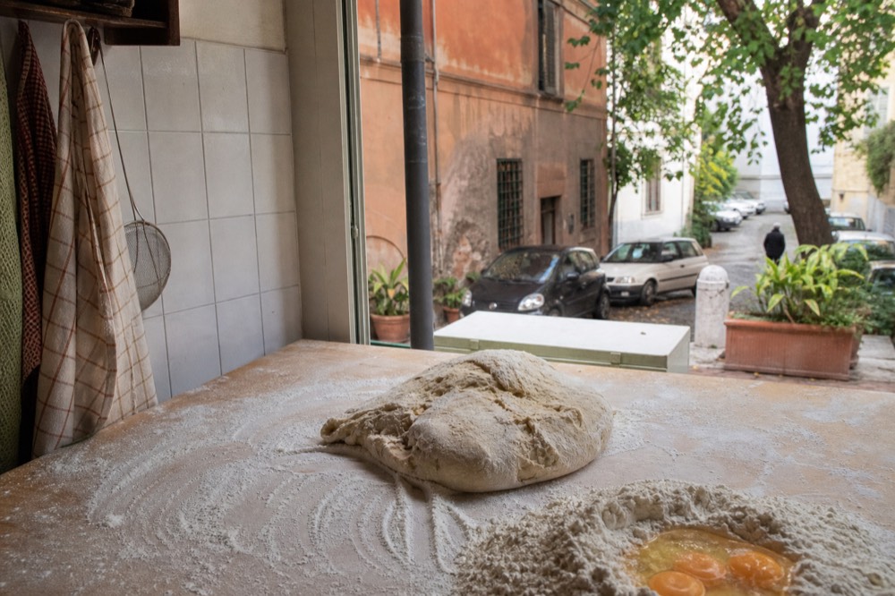 Hands kneading pasta dough on a floured wooden workbench