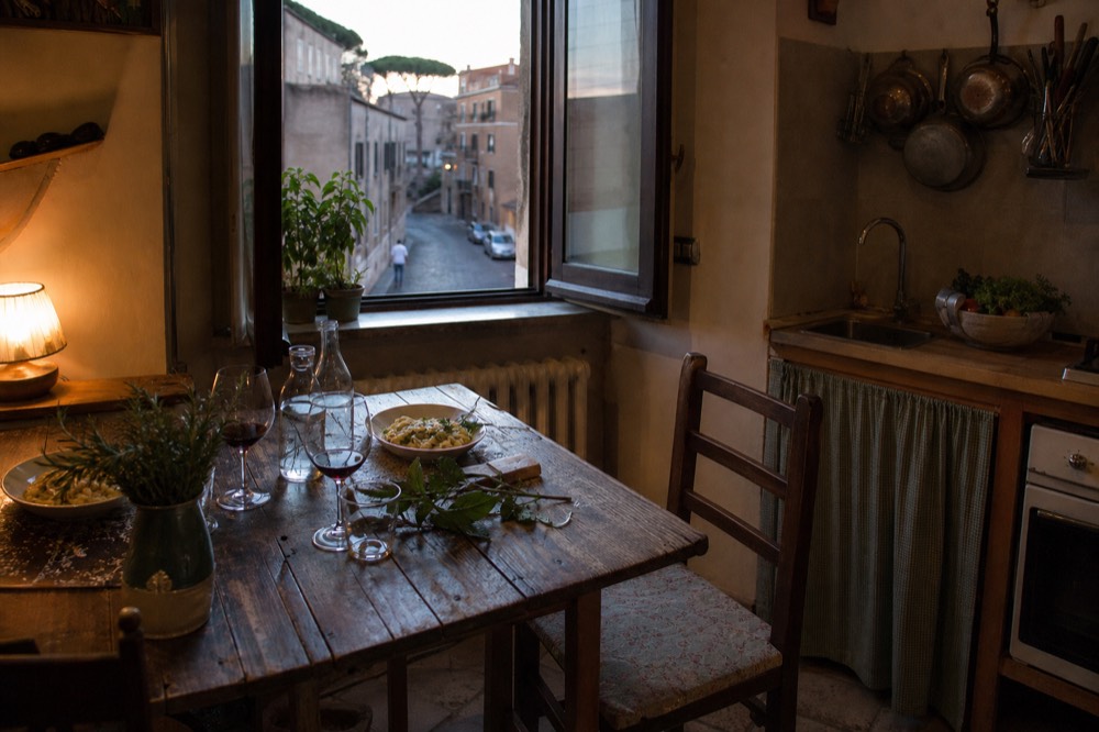 A rustic kitchen table set with pasta plates, wine glasses and fresh herbs
