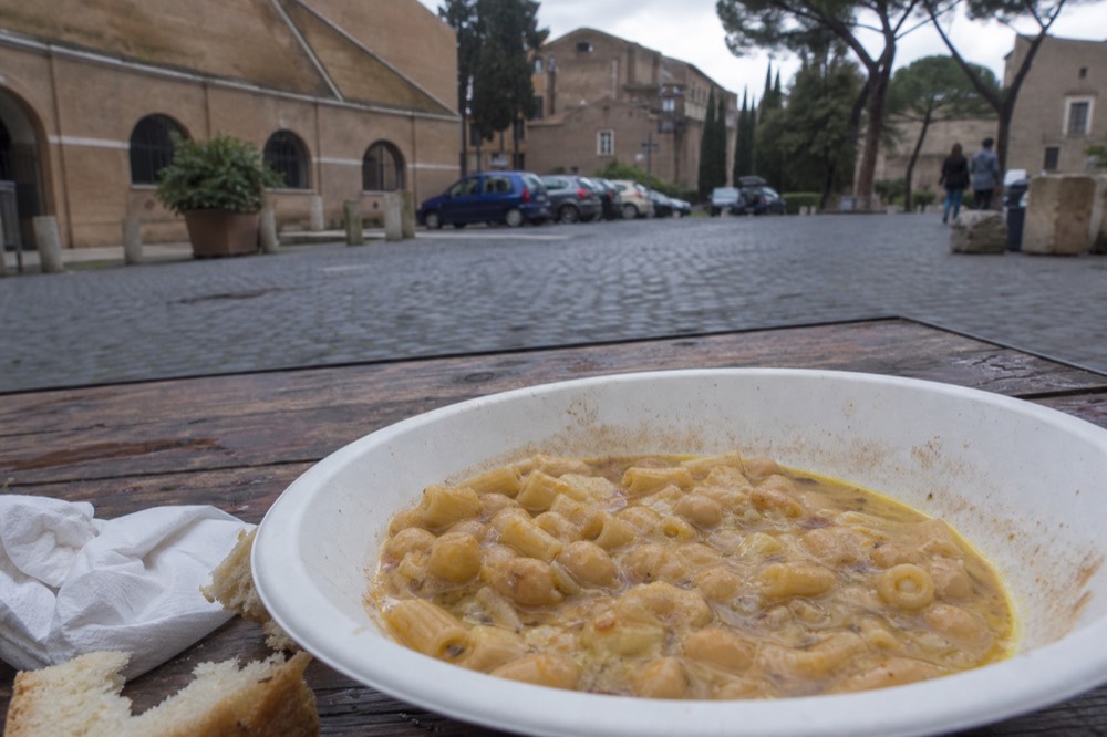 A bowl of chickpea and pasta soup with olive oil on a wooden table