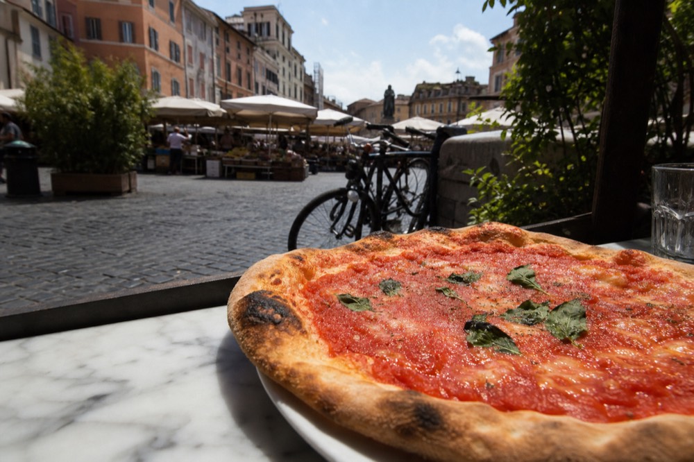 Thin crust marinara pizza with tomato and basil on a marble counter