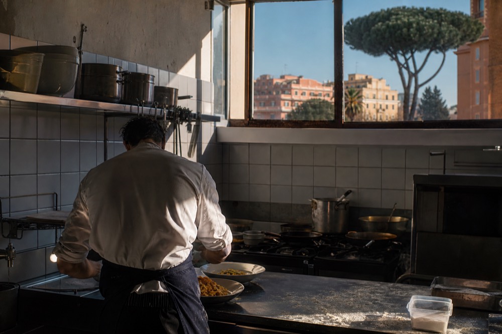 Chef plating fresh pasta in a small Roman restaurant kitchen before evening service