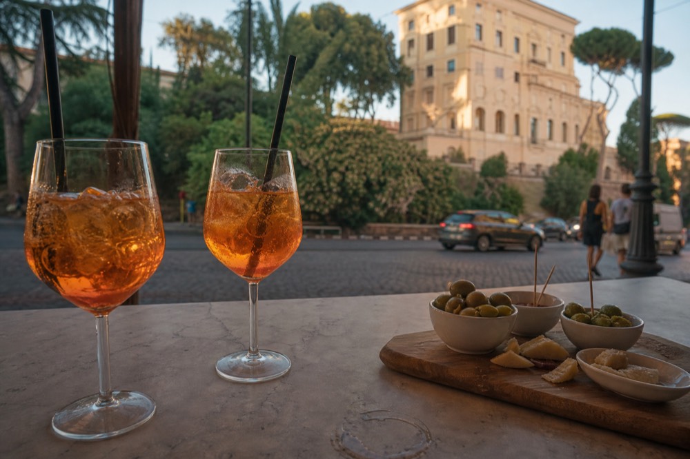 Two glasses of spritz and a small snack board on a marble bar counter