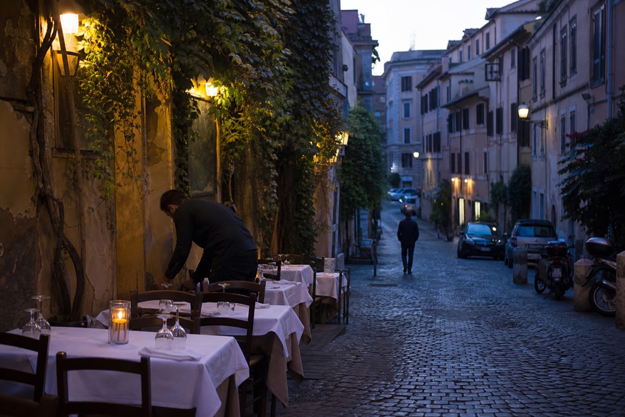 Evening light over a Roman street with restaurant tables set for dinner