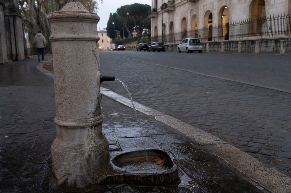A stone drinking fountain on a Rome sidewalk with water flowing