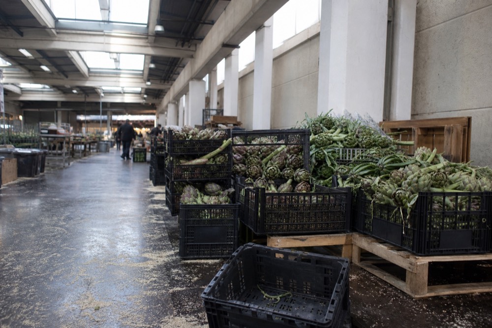 A market stall display with fresh vegetables and crates in a covered Rome market