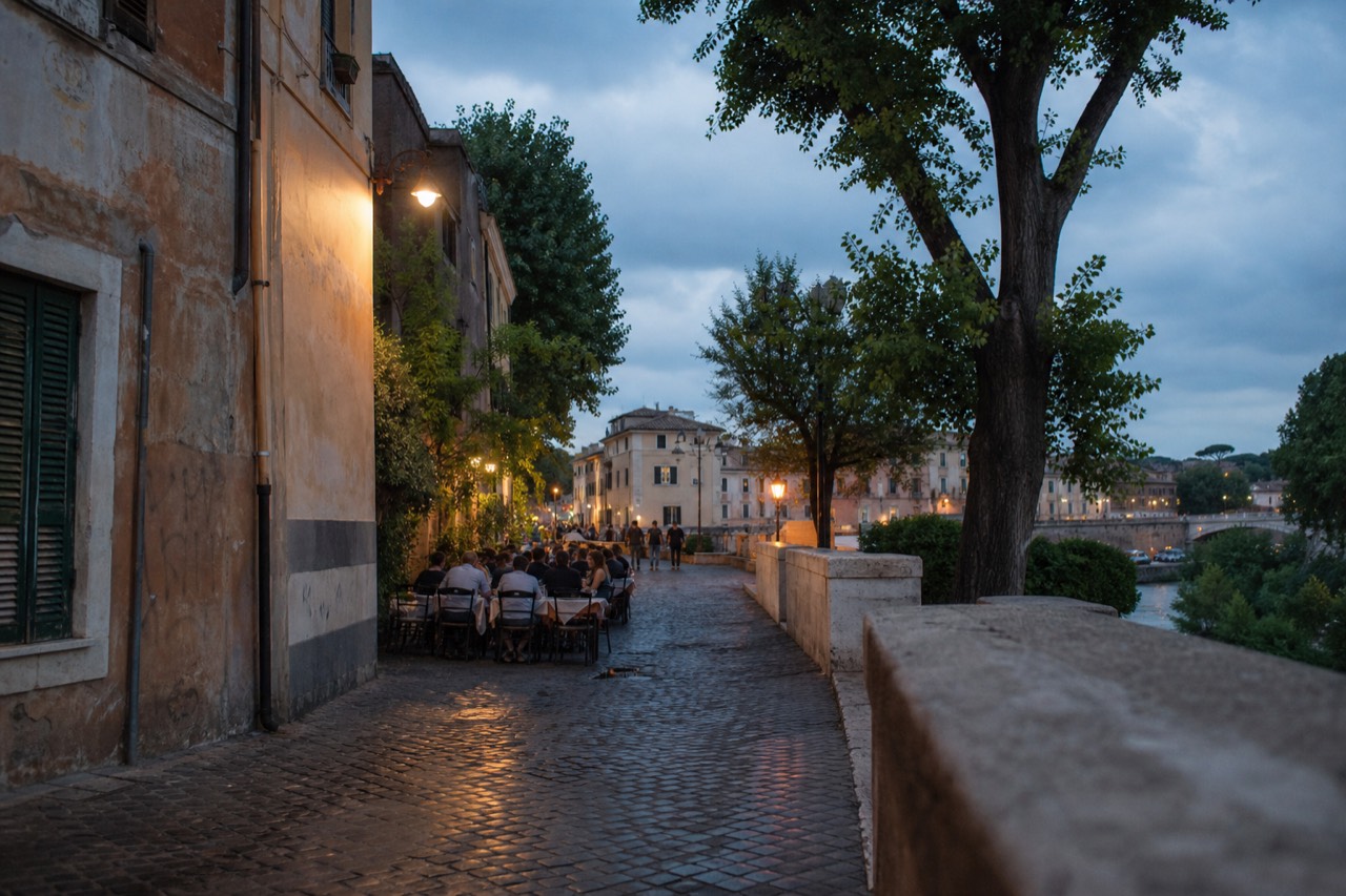 A narrow Rome street with restaurant tables set out in the evening