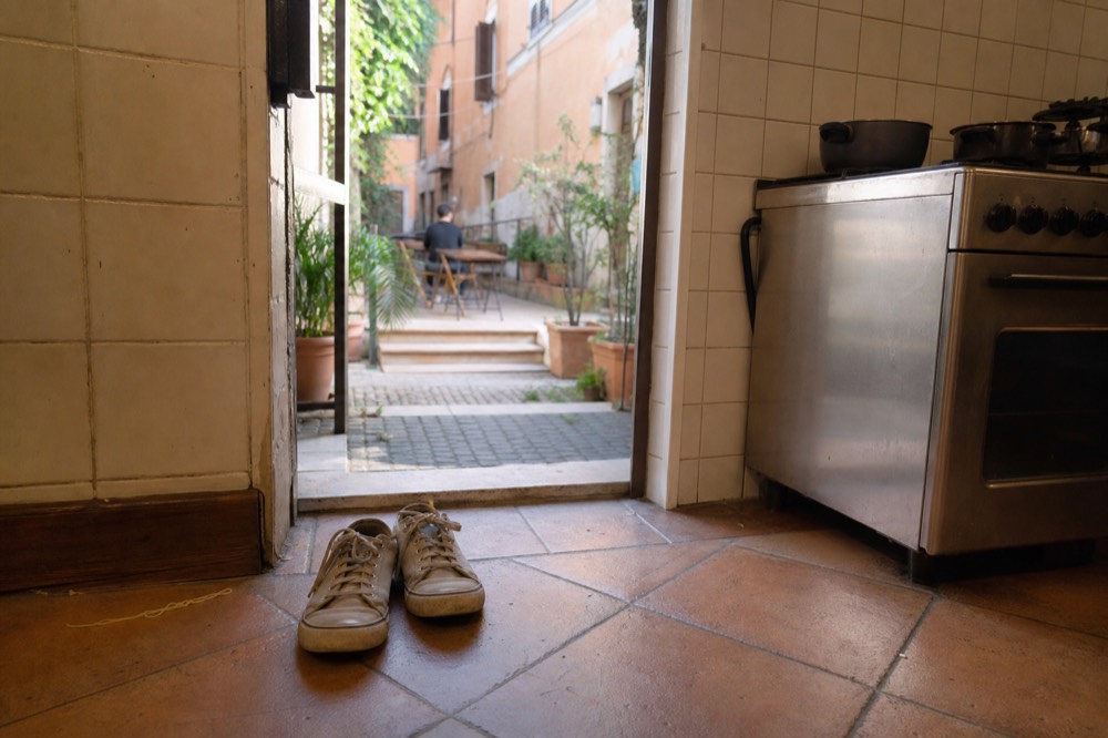A pair of plain canvas shoes on a tiled kitchen floor beside a stove