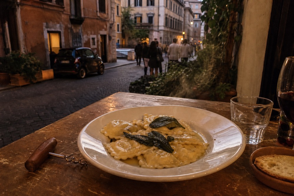 A plate of ravioli with melted butter and sage leaves on a rustic wooden table