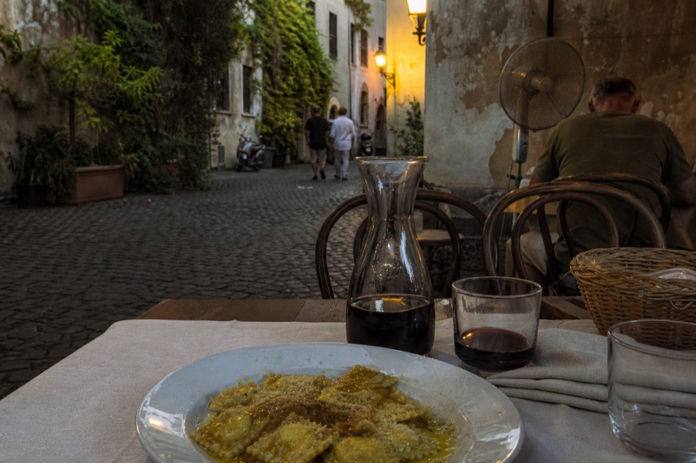 A rustic trattoria table set with white plates, a carafe of red wine and a linen napkin