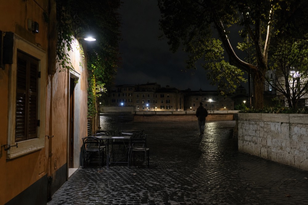 Night-lit alley in Trastevere with closed shutters and empty outdoor tables before the evening crowd