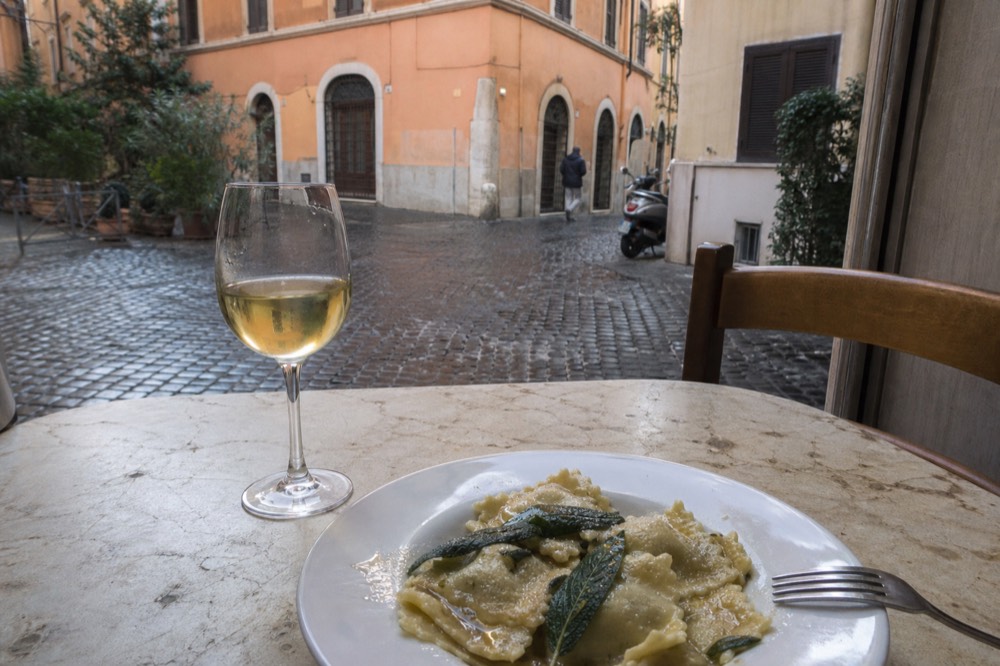 Fresh ravioli with sage butter sauce plated on a white dish beside a fork and glass of white wine
