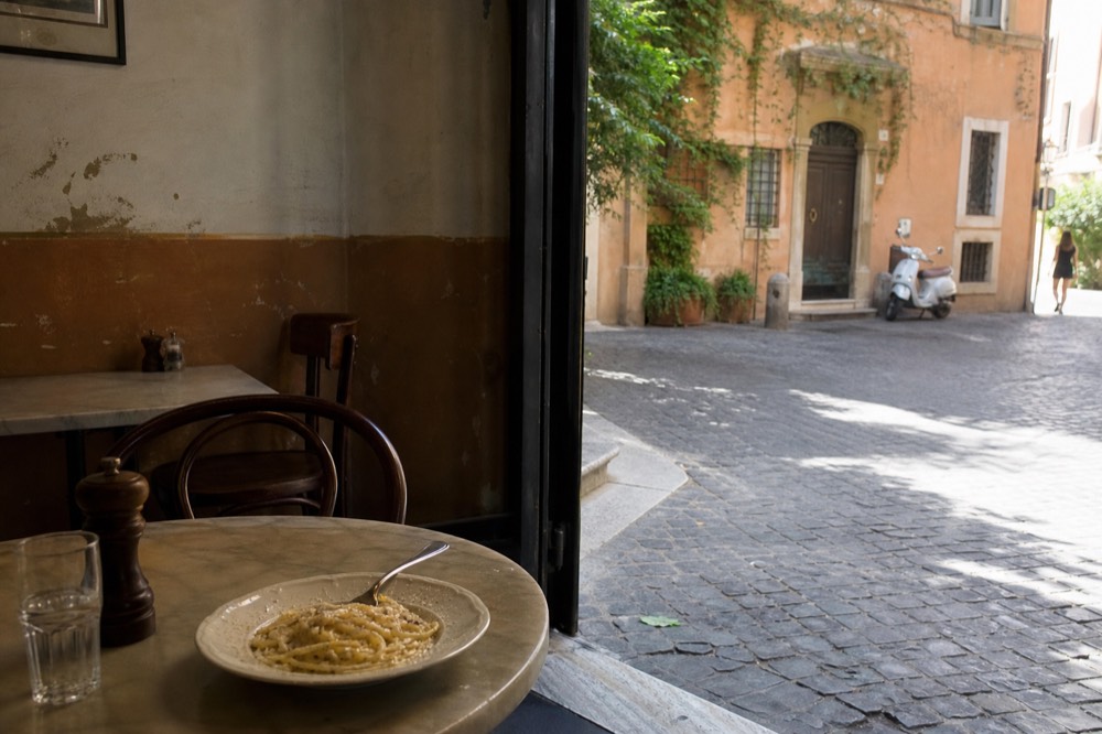 A rustic Roman trattoria interior with marble-topped tables, bentwood chairs and a chalkboard menu