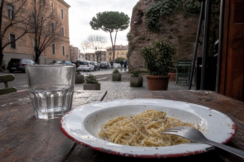 A plate of cacio e pepe pasta with black pepper and grated pecorino on a rustic table