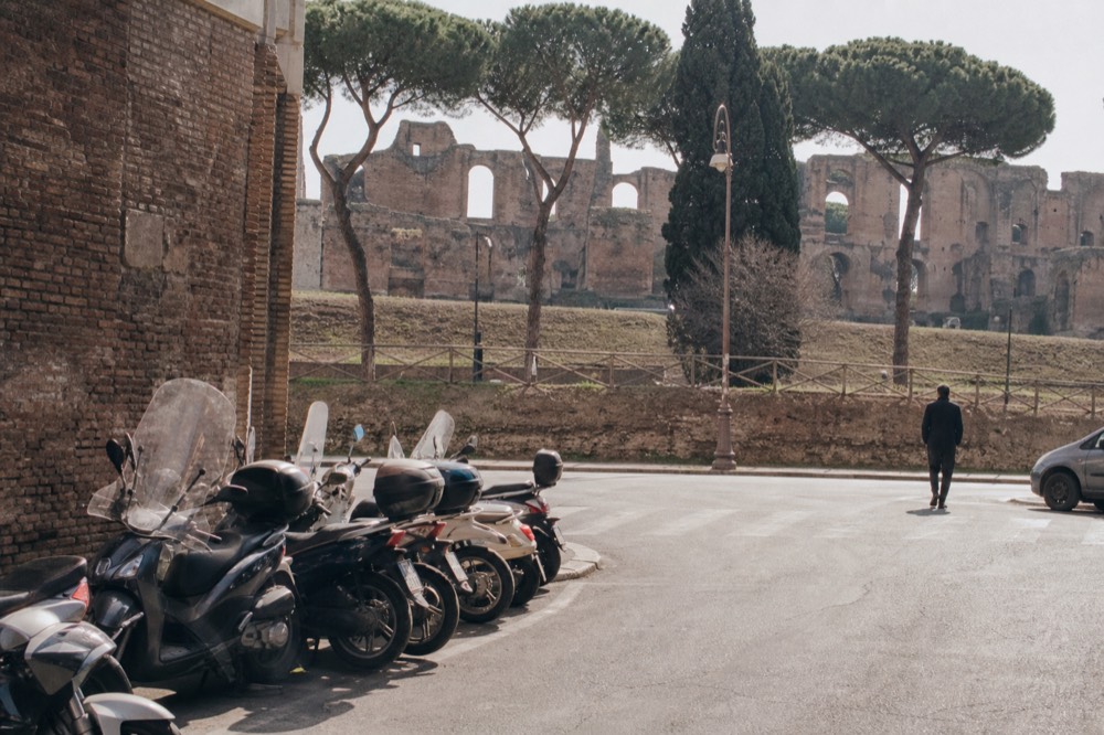 A Rome street corner near the Circus Maximus with stone ruins visible behind parked scooters