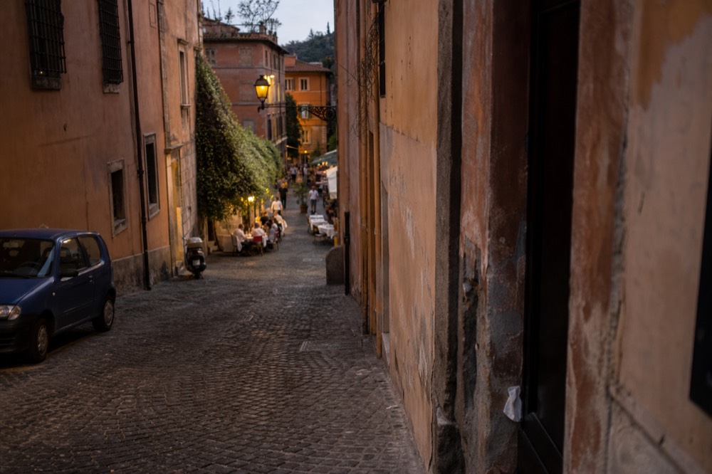 An evening street in Trastevere with warm lights over restaurant tables and cobbled pavement