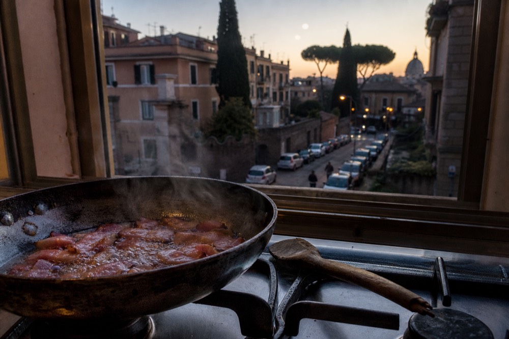 Thin ribbons of guanciale frying in a steel pan until the edges crisp