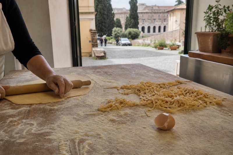 Fresh pasta being rolled and cut on a floured wooden board during a cooking class in Rome, Italy