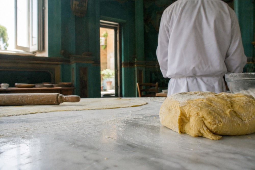 Hands kneading pasta dough on a floured marble surface in a Rome cooking school