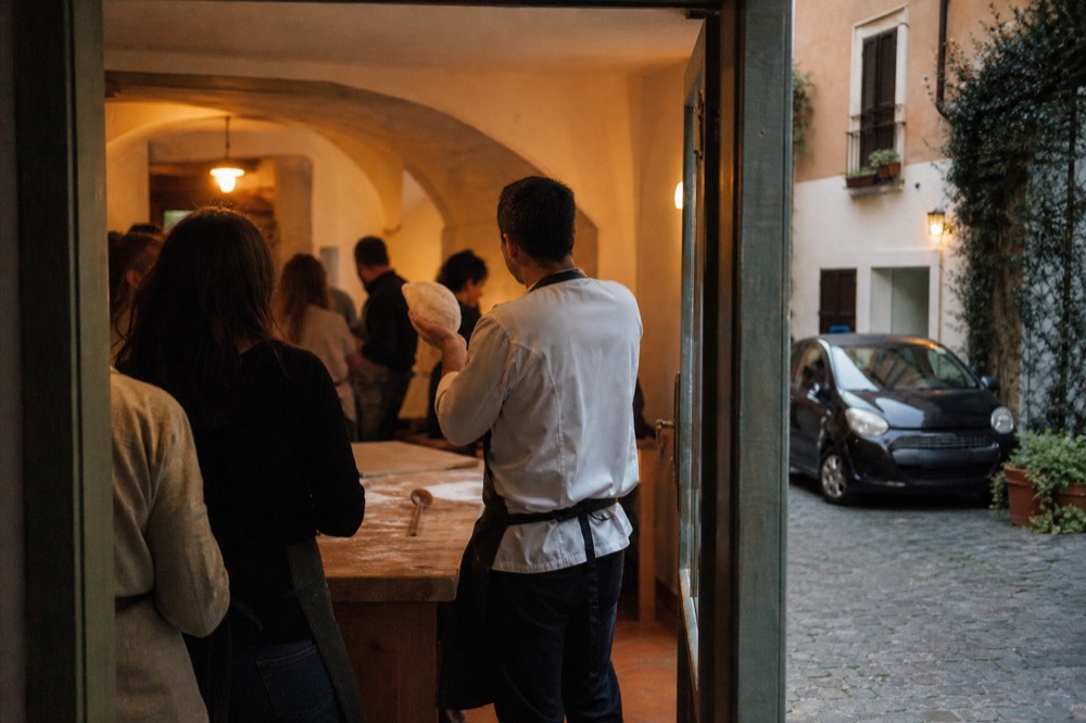 A cooking instructor explaining pasta dough to a small group around a kitchen island in Rome