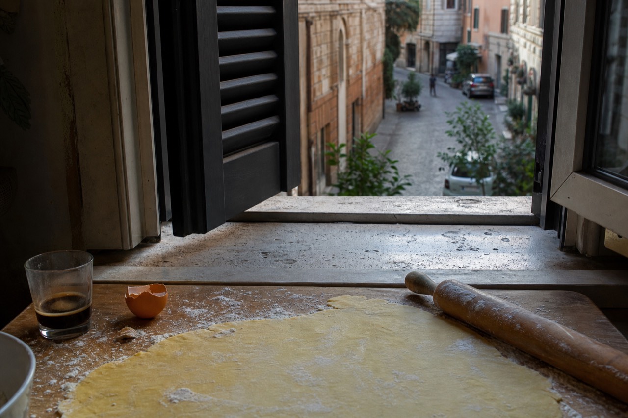 Fresh egg pasta dough being rolled by hand on a wooden board in a Roman kitchen