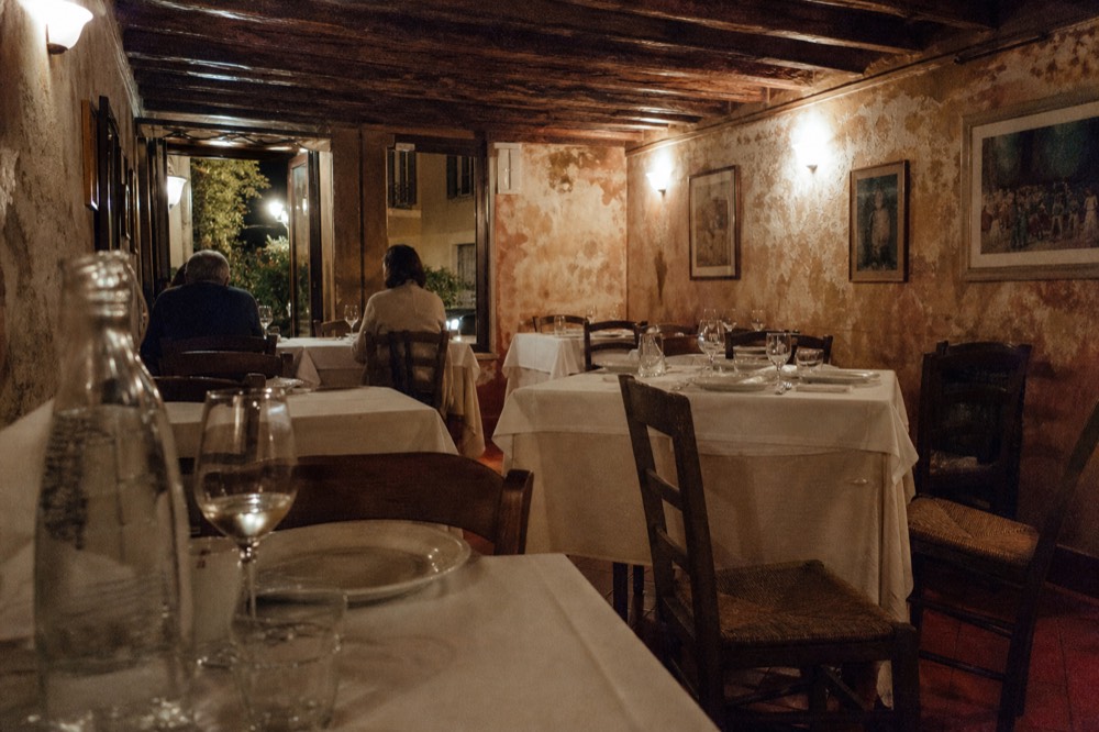 A trattoria dining room at night with tables set with white plates and wine glasses