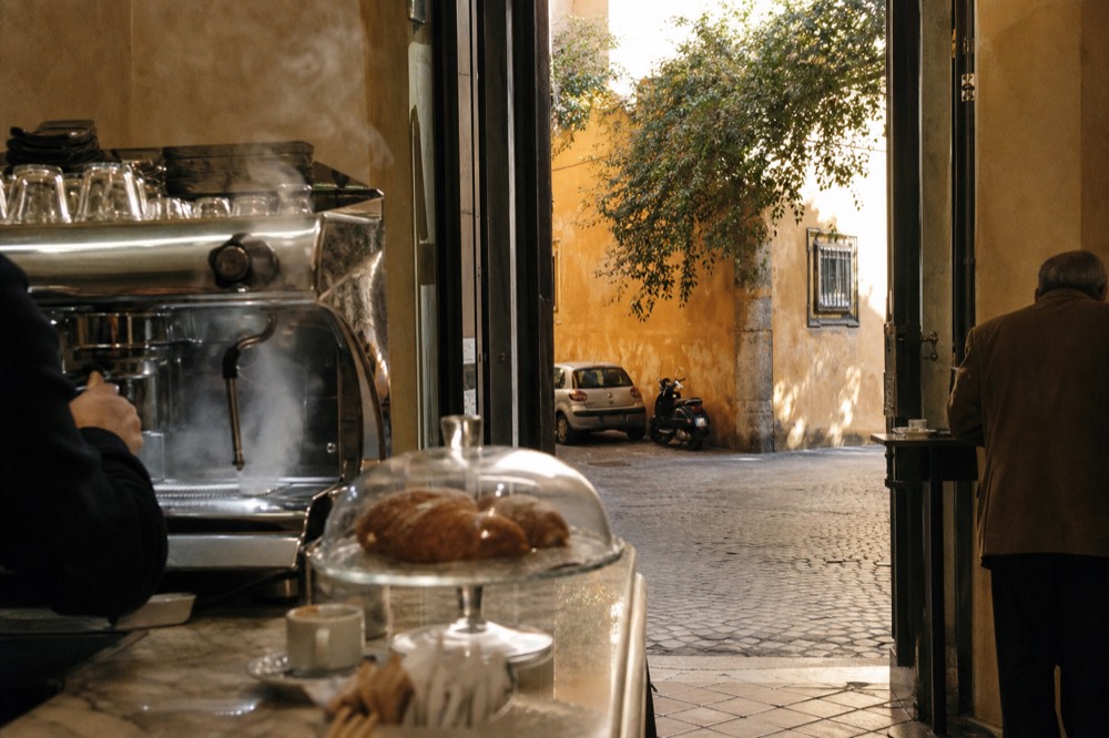 A Rome bar counter with a chrome espresso machine and pastries under glass in the morning