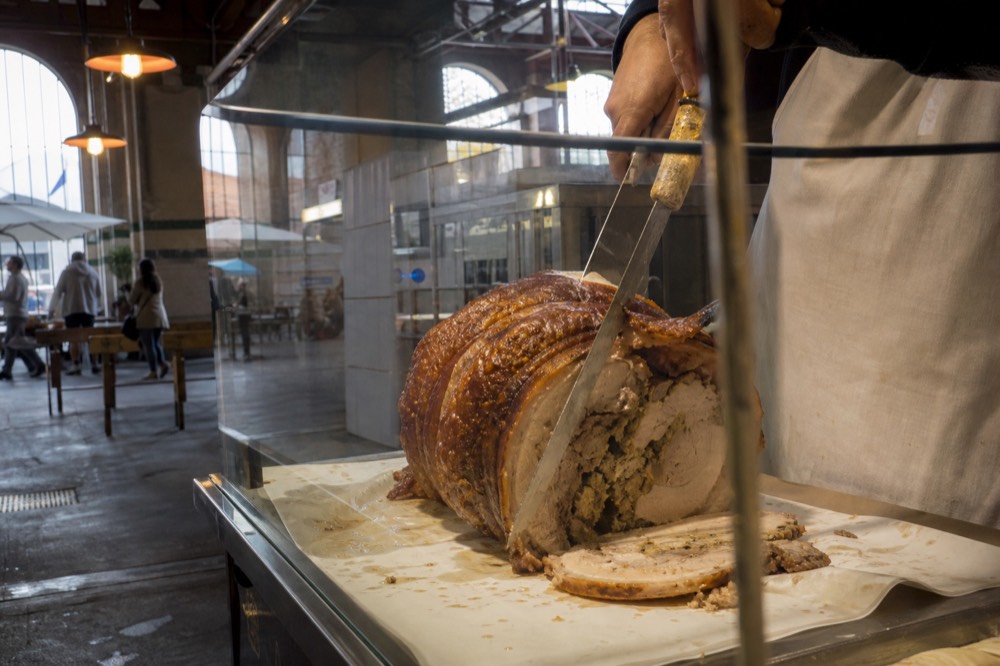 A market stallholder slicing porchetta behind a glass case in a Rome market