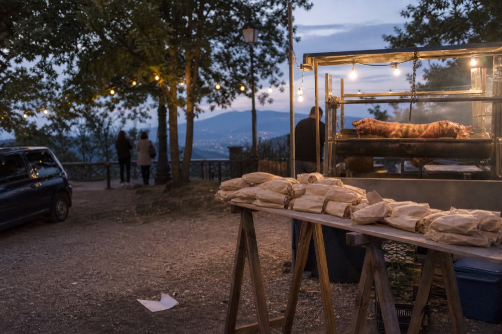 An outdoor food festival stand with roasted pork and paper-wrapped sandwiches under string lights
